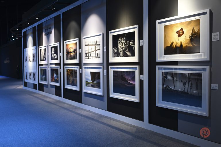 Framed digital art and photographs displayed on a gallery wall under soft lighting.