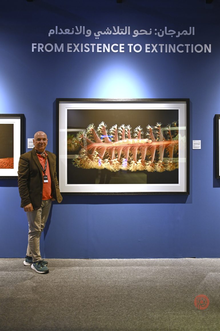 A man stands beside coral artwork under a sign that reads FROM EXISTENCE TO EXTINCTION in English and Arabic.