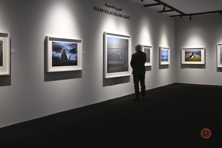 A person views framed landscape photos on display in an art gallery titled Eilean Solas (Island Light).
