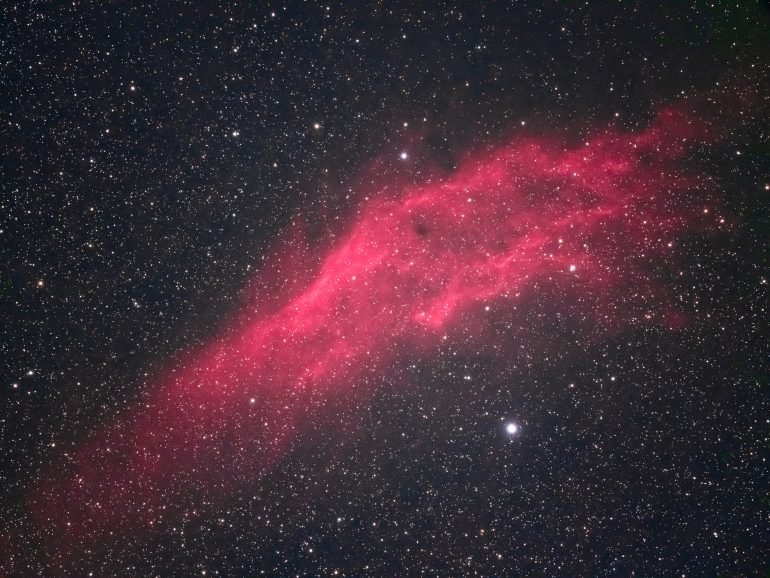 A bright pink nebula stretches diagonally across a star-filled night sky.