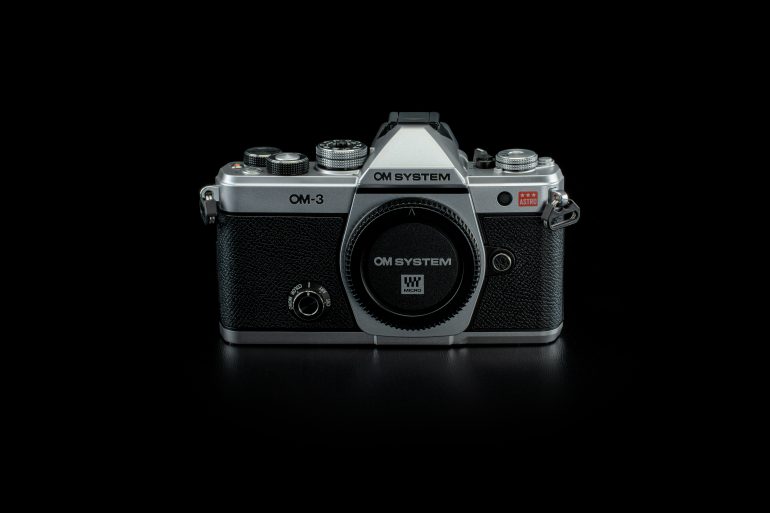 Vintage OM System OM-3 camera with a black body and silver accents, displayed against a black background.