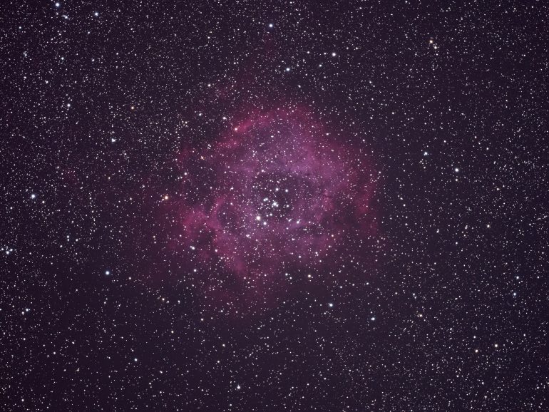 Pink nebula surrounded by countless stars against a dark sky background in outer space.