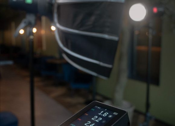 A close-up of a camera and flash trigger setup, with a softbox and light stand in the background.