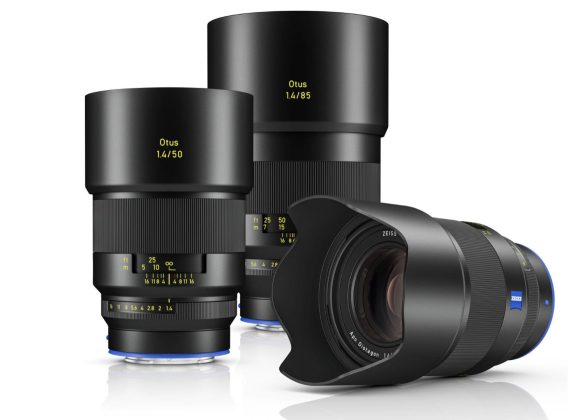 Three Zeiss Otus camera lenses, two standing upright and one lying on its side with a lens hood attached.