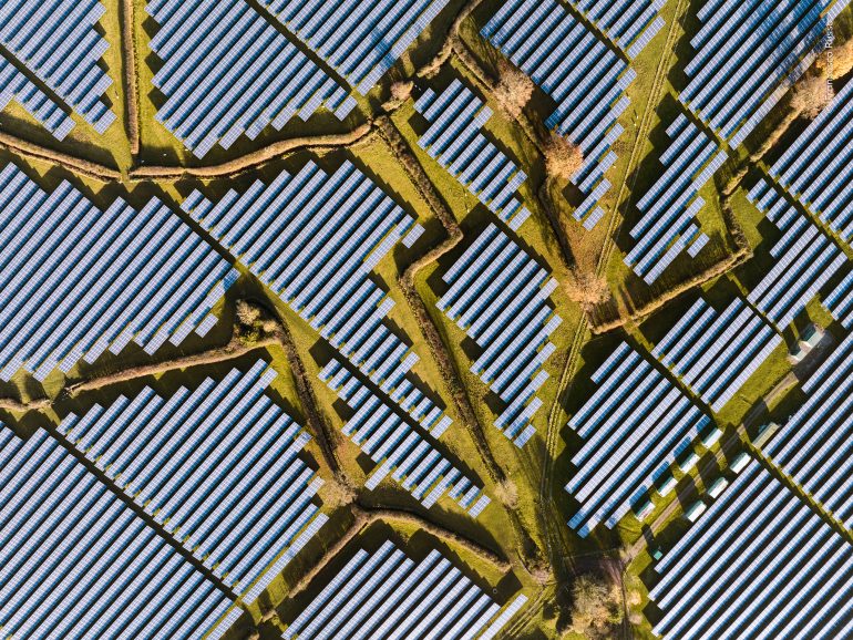 Aerial view of a solar farm with rows of solar panels separated by grassy paths.