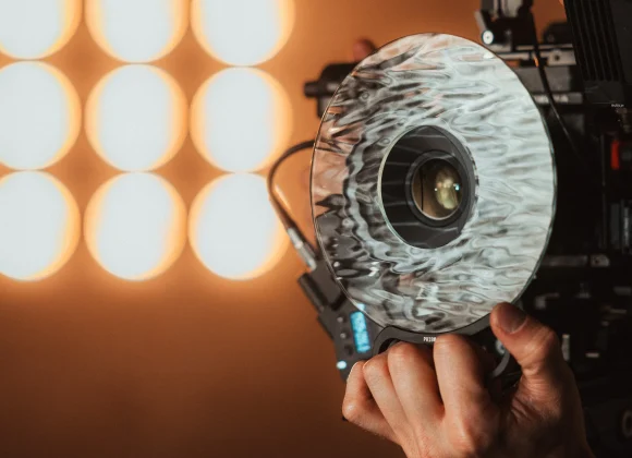 A hand adjusts a professional movie camera with studio lights glowing softly in the blurred background.