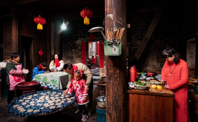 Family preparing food together in a warmly lit traditional kitchen decorated with red lanterns and festive ornaments.