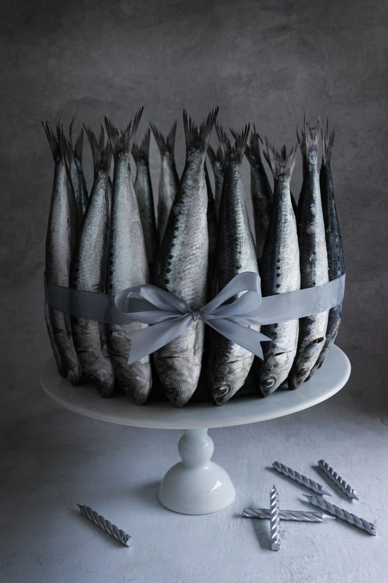 A group of upright fish tied with a gray ribbon on a cake stand, with candles scattered nearby.