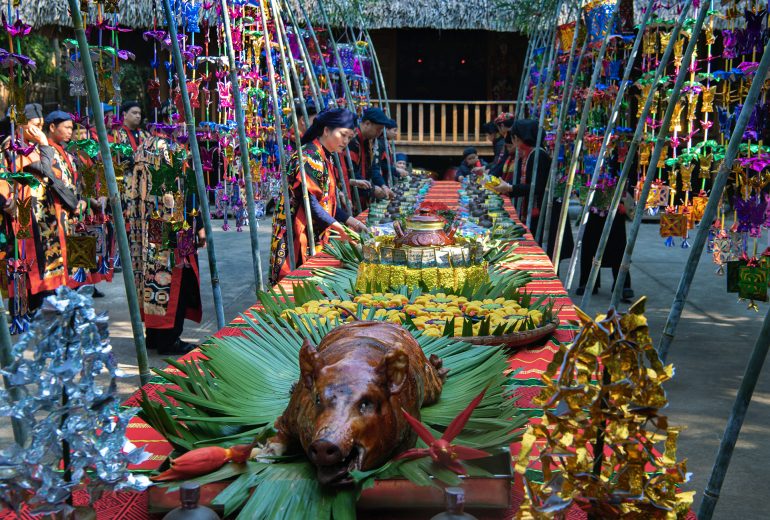 A long feast table with a roasted pig, surrounded by people in colorful traditional clothing and decorations.