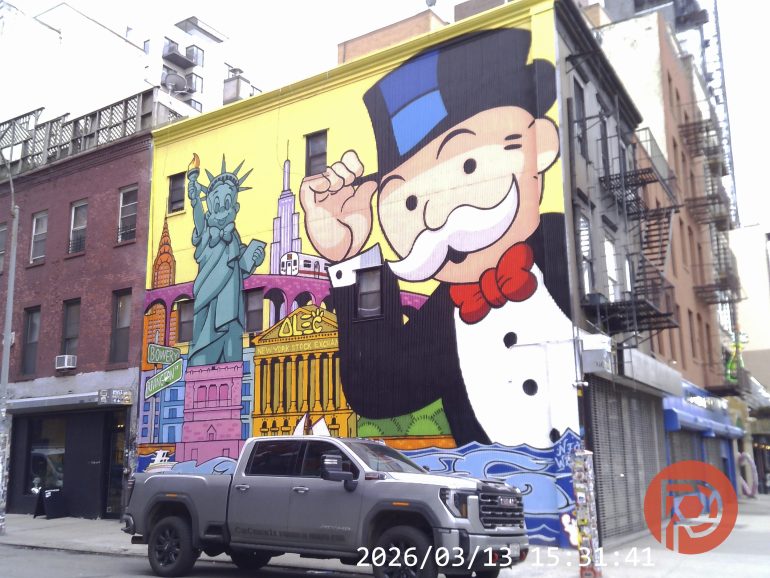 Colorful mural of Monopoly Man, Statue of Liberty, and NYC landmarks on a city building, truck parked in front.