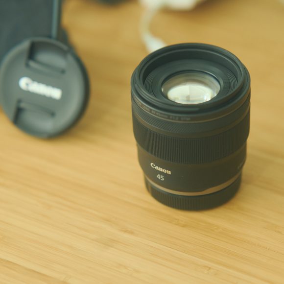 A Canon 45mm camera lens on a wooden surface, with a lens cap and phone in the background.