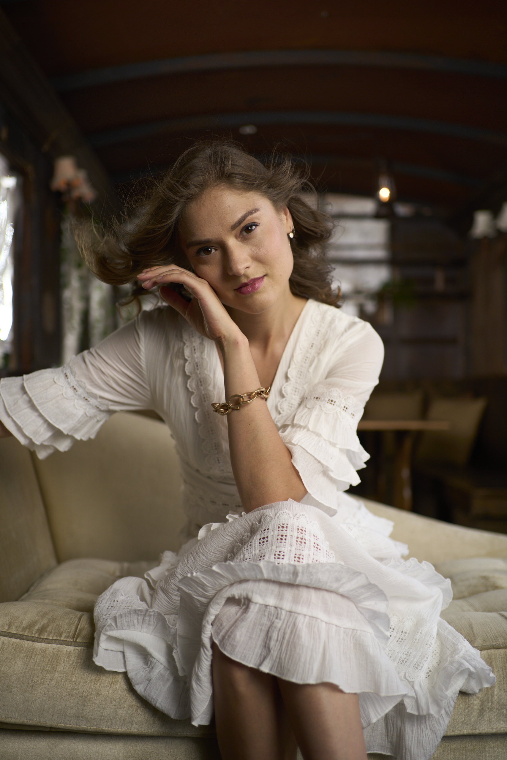 Why Your Lightroom Presets Look Fake (And What Actually Works) A woman in a white dress sits on a sofa, resting her head on her hand and smiling slightly.