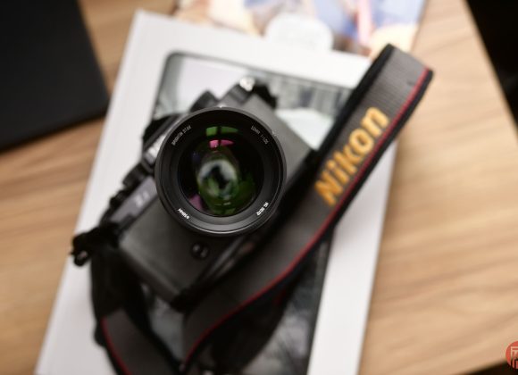 A Nikon camera with a lens and strap rests on a book on a wooden surface.