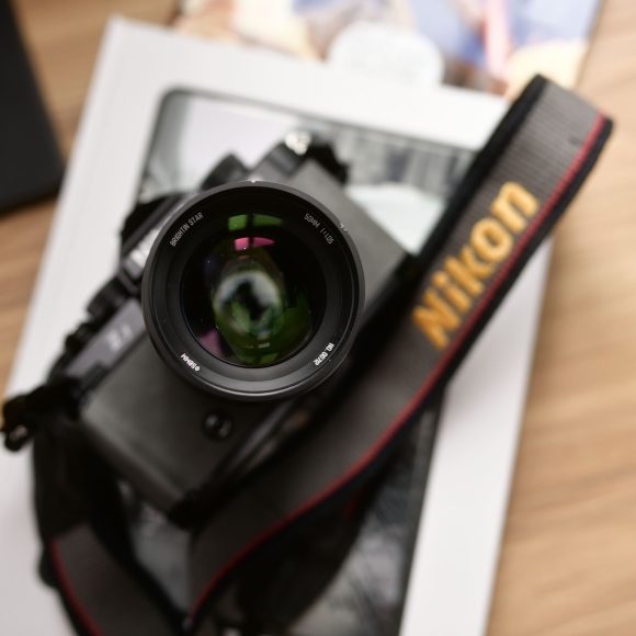 A Nikon camera with a lens and strap rests on a book on a wooden surface.