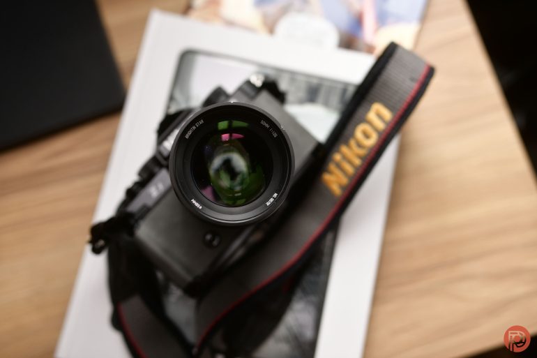 A Nikon camera with a lens and strap rests on a book on a wooden surface.