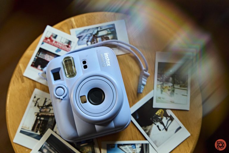 A blue Instax camera on a wooden table surrounded by several instant photos.