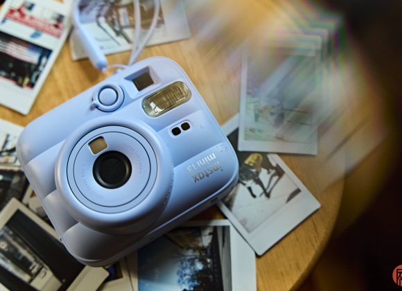 A blue Instax Mini 11 camera on a table, surrounded by several instant photos.