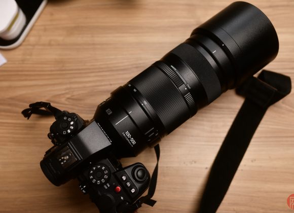 A black camera with a large 100-400mm zoom lens rests on a wooden surface.