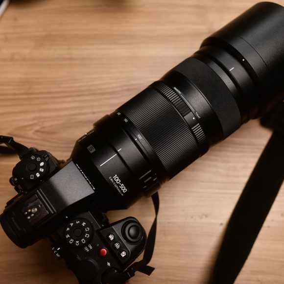 A black camera with a large 100-400mm zoom lens rests on a wooden surface.