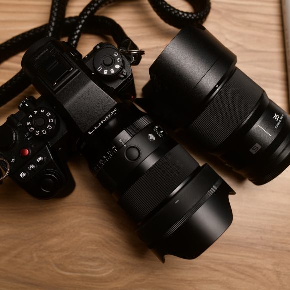 A black digital camera with a lens attached, next to an additional lens on a wooden surface.