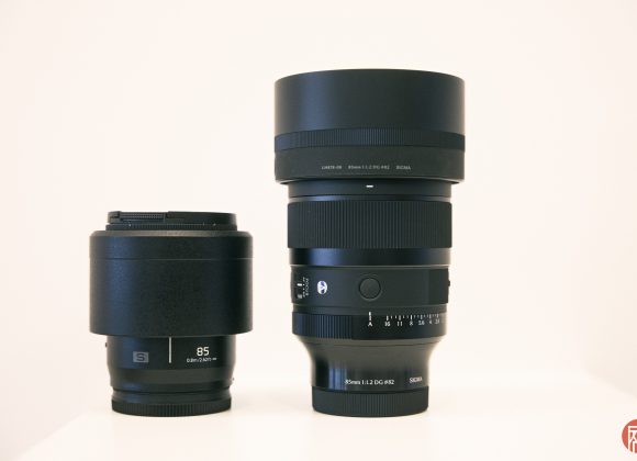 Two black camera lenses, one shorter marked 85, and a taller Sigma lens, both on a white surface.