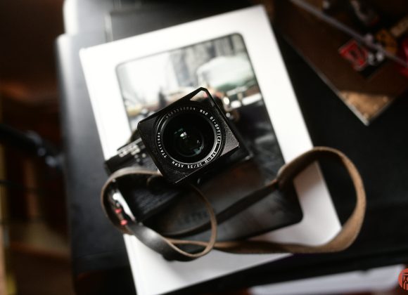 A camera with a brown strap rests on top of a book with a blurred city photograph on its cover.