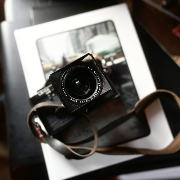 A camera with a brown strap rests on top of a book with a blurred city photograph on its cover.