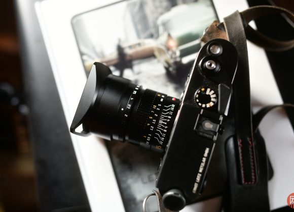 A black camera with a lens rests on a book featuring a vintage photo of cars in the background.