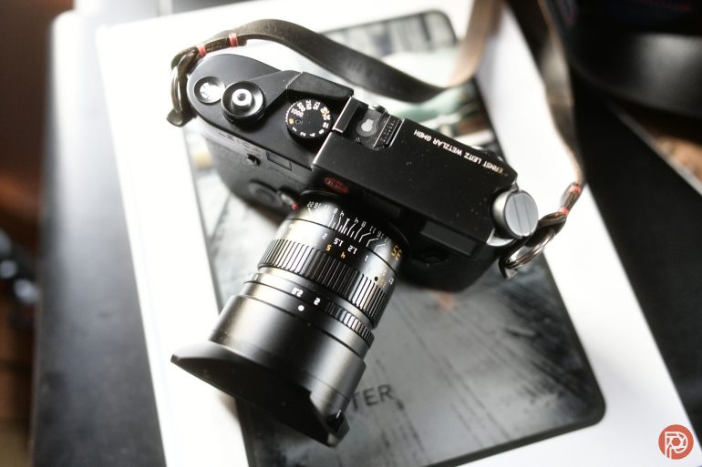 A black Leica camera with a lens, resting on top of a closed book.