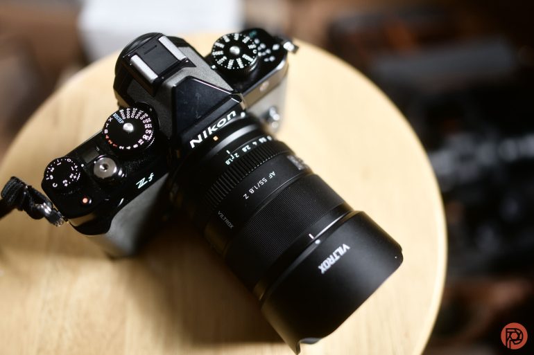 A Nikon Z fc camera with a Viltrox lens rests on a light wooden surface.