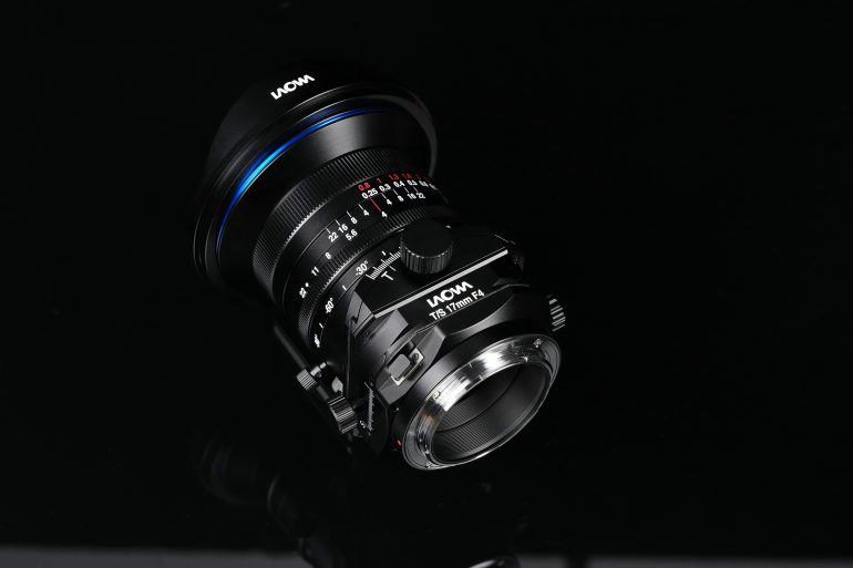 A Laowa camera lens with manual focus and aperture rings, displayed on a black reflective surface.