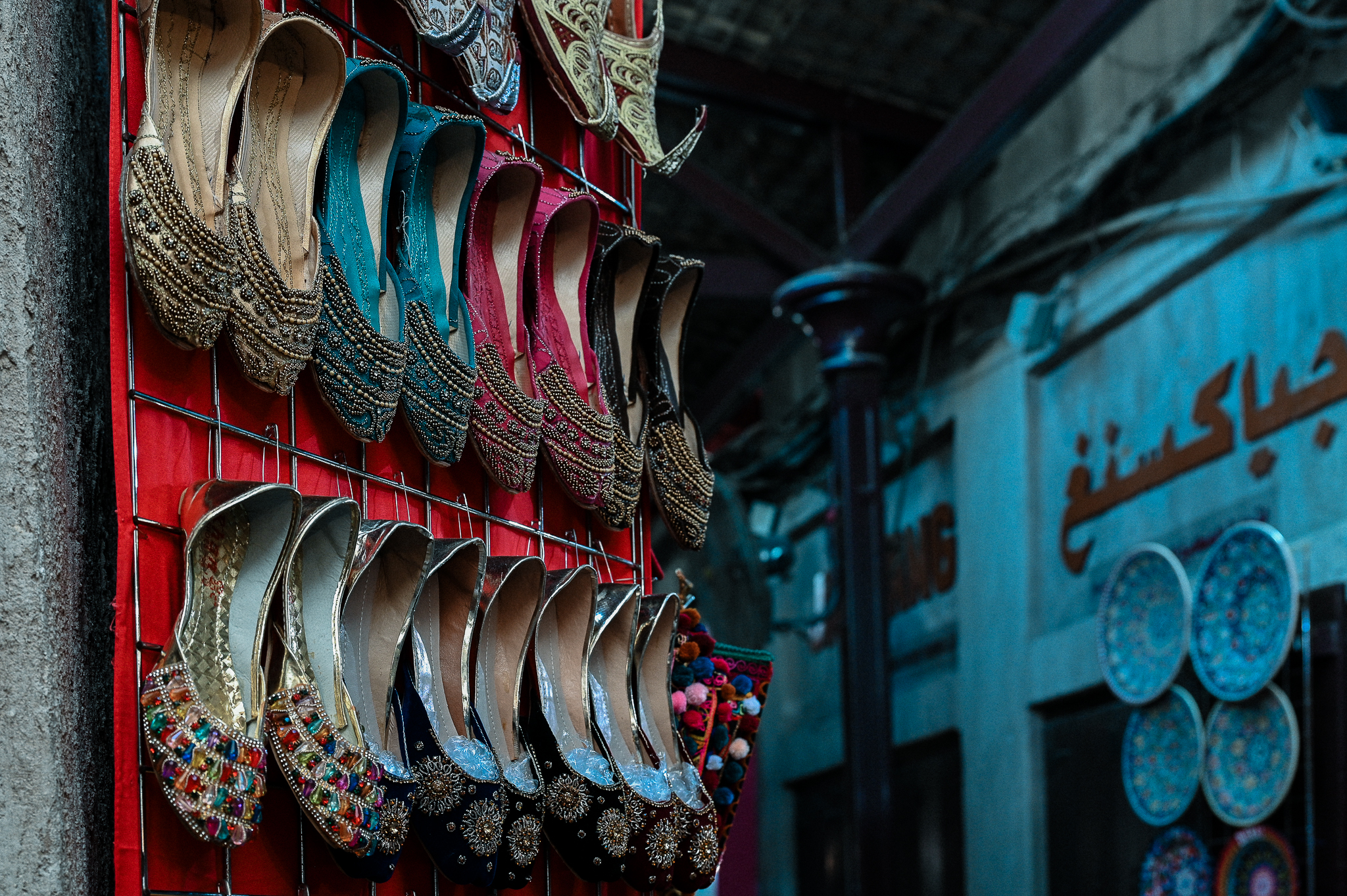 Traditional embroidered shoes in various colors displayed on a red rack at an outdoor market or bazaar.