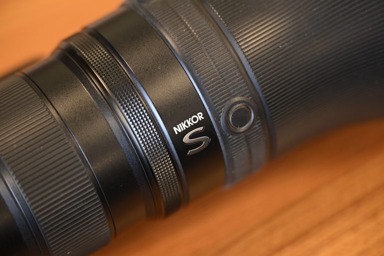 Close-up of a black NIKKOR S camera lens on a wooden surface.
