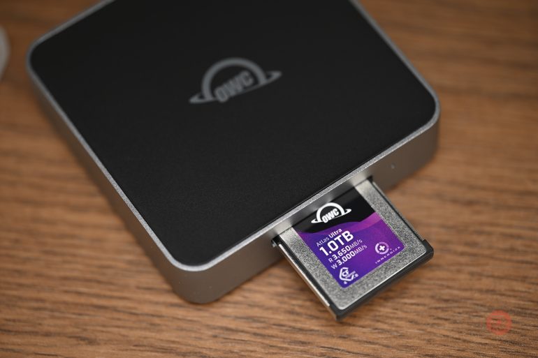 A 1TB OWC memory card partially inserted into a black card reader on a wooden surface.