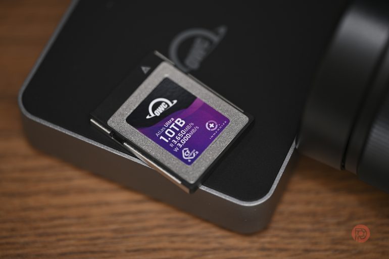 A 1TB OWC memory card on a black device, placed on a wooden surface with part of a camera visible.