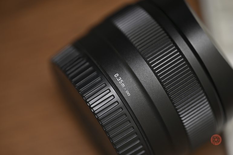Close-up of a black camera lens showing focus rings and a 0.35m–infinity marking, on a brown surface.