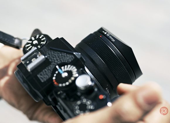 Close-up of a person holding a black digital camera with a lens and dials in focus.