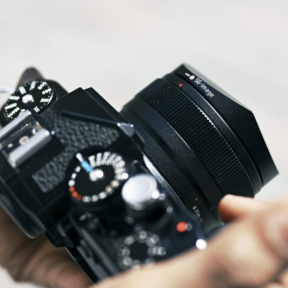 Close-up of a person holding a black digital camera with a lens and dials in focus.