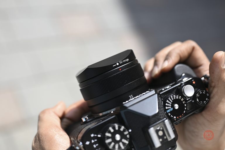 Close-up of hands holding a camera, adjusting the lens and dials outdoors.