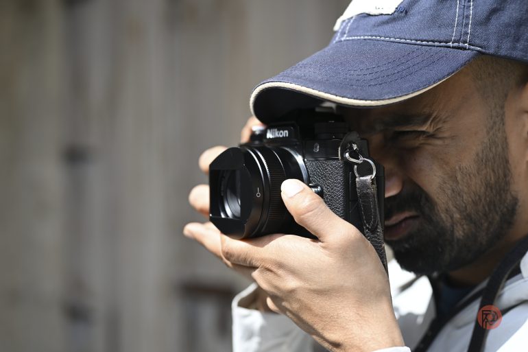 A man in a blue cap is taking a photo with a Nikon camera, focusing intently.