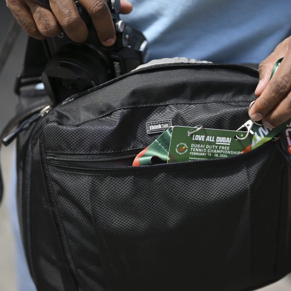 A person pulls a Dubai tennis championship lanyard from a black camera bag.
