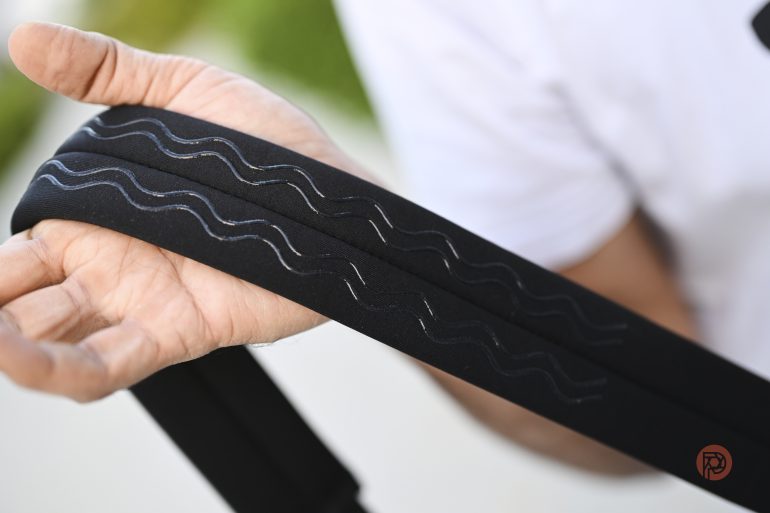 A person holding a black strap with wavy silver lines and a small red circular logo on the end.
