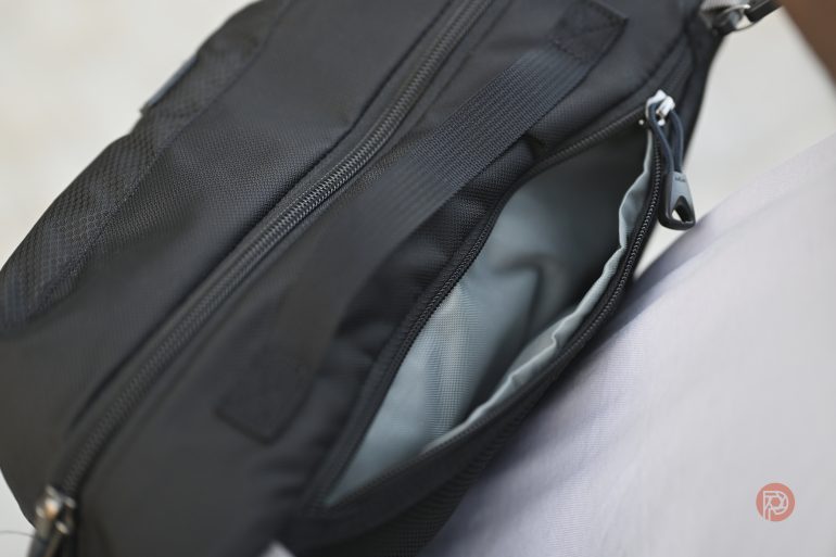 A close-up of an open black bag with a zippered compartment and a light gray inner lining.