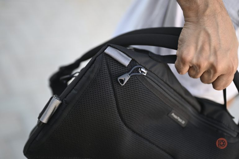 Close-up of a person holding a black backpack by the handle, with a visible zipper and mesh fabric.
