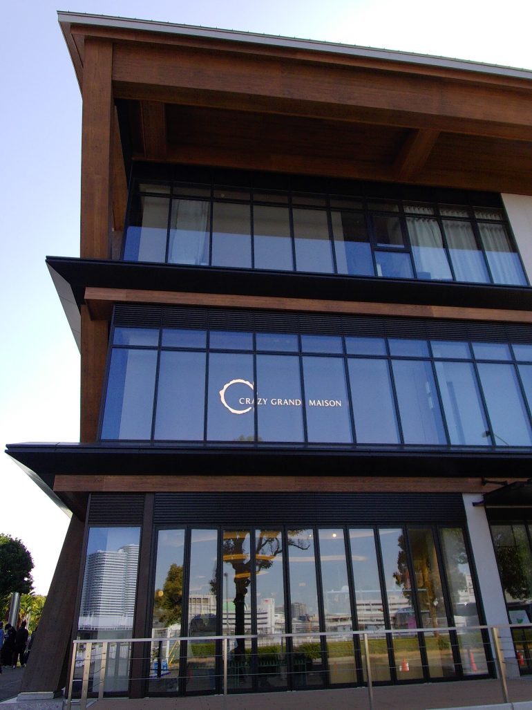 A modern, multi-story building with large windows and a sign reading CRAZY GRAND MAISON.