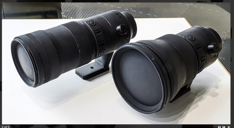Two large black camera lenses with mounting feet placed side by side on a white surface.