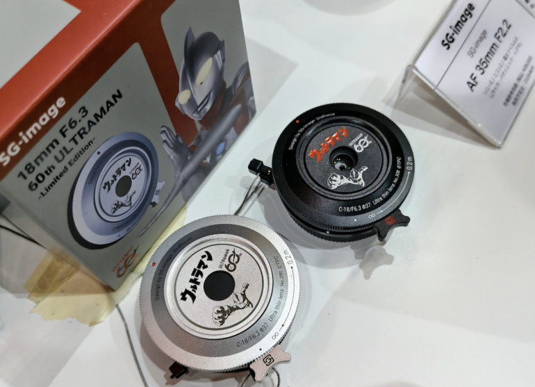 Two Ultraman-themed camera lenses and their box displayed on a white surface at an exhibition.