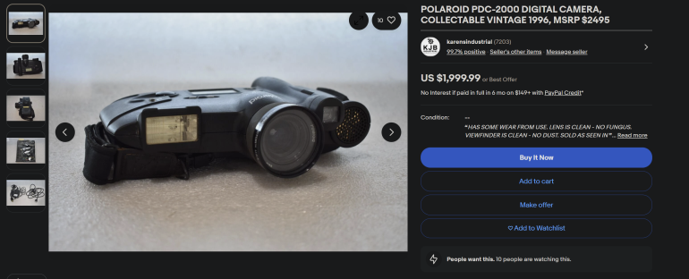 A vintage Polaroid PDC-2000 digital camera sits on a white surface, shown from a side angle.