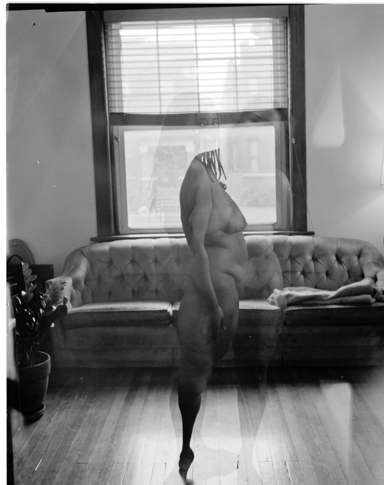 Black and white photo of a nude person standing in front of a couch, with a ghostly double exposure effect.
