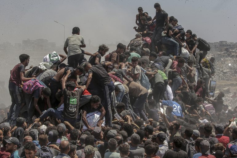 A large crowd of people tightly packed together, some climbing atop others, in a dusty outdoor setting.